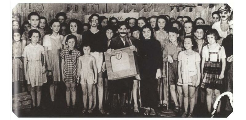 Szene aus einem deutschen Propagandafilm mit dem Ensemble der Kinderoper Brundibár. Eva ist vermutlich das Mädchen im Faltenrock vorne rechts. Die meisten der Kinderdarsteller/-innen wurden kurz nach der letzten Aufführung nach Auschwitz-Birkenau deportiert und ermordet.