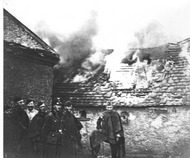 Foto von einem brennenden Haus, davor stehen mehrere SS-Männer